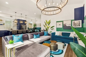 A modern living room with a sectional sofa, ottomans, a coffee table, and a dining area with chairs. - TWO full houses with a private pool, hot tub, gym, sauna, massage chair, cold plunge, movie projector, astroturf, axe throwing, corn hole and other lawn games! Unwind in this relaxing Paradise Oasis and let your worries drift away! (Austin)
