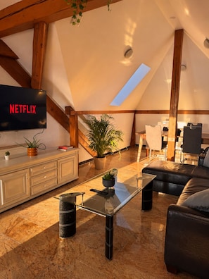 A modern living room with a flat-screen TV, a glass coffee table, a sofa, and a dining area with chairs. - Vrbo Property (Basel)