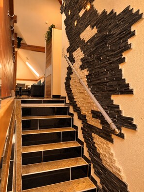 A staircase with a unique black and beige patterned wall, a metal handrail, and a wooden floor. - Vrbo Property (Basel)