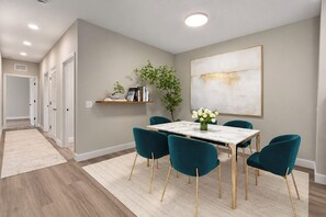 Un comedor con una mesa de mármol, sillas color turquesa, un jarrón blanco con flores y un cuadro abstracto de gran tamaño en la pared.