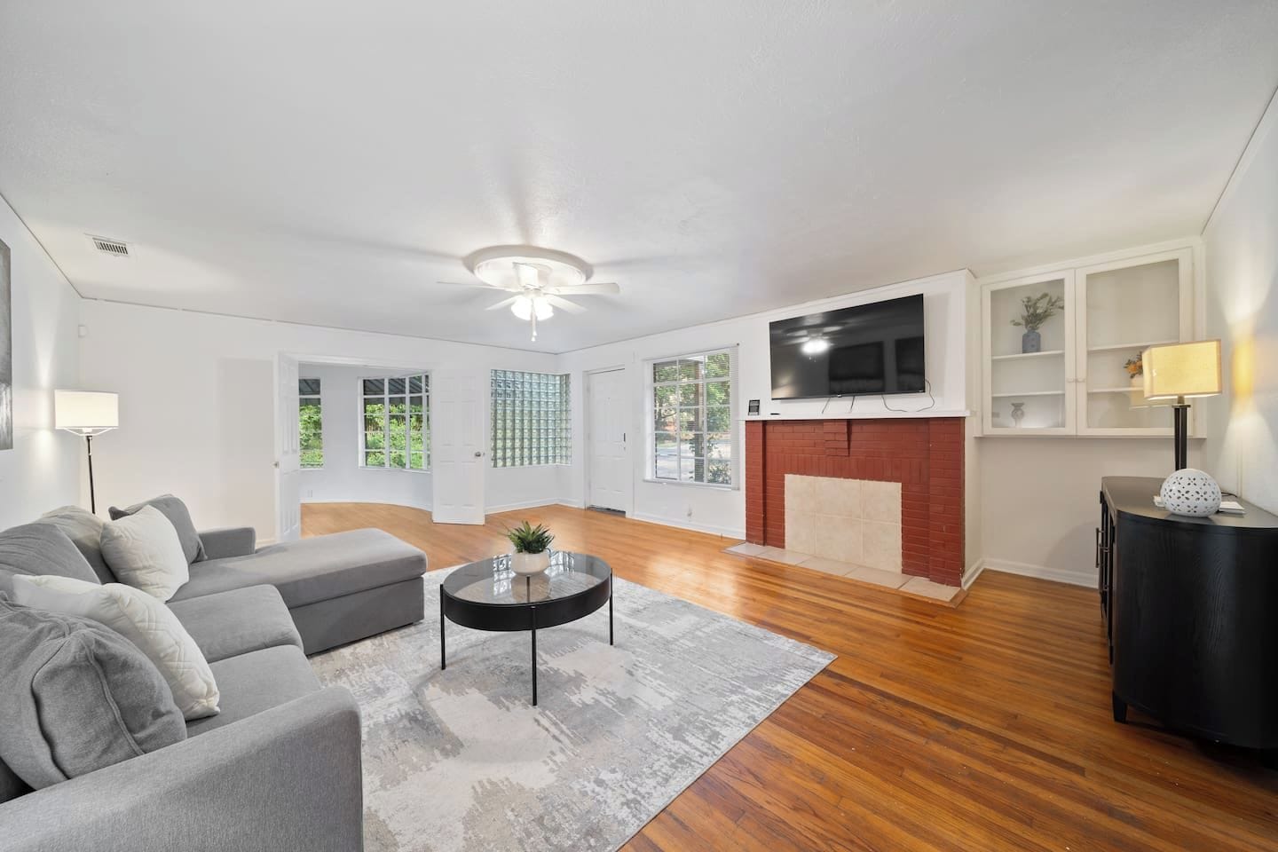 Een moderne woonkamer met een grijze bank, een ronde salontafel en een open haard.