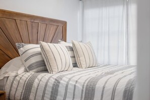 A bed with striped bedding and multiple pillows, a wooden headboard, and a window with sheer curtains. - 4BR House Near FSU, Pet-Friendly (Tallahassee)