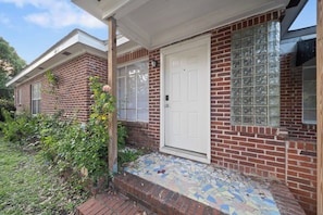 A two-story brick house with a white door and windows, a small porch with a tiled floor, and a garden with plants and a rose bush. - 4BR House Near FSU, Pet-Friendly (Tallahassee)