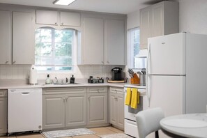 A kitchen with white cabinets, a dishwasher, a coffee maker, and a refrigerator. - 4BR House Near FSU, Pet-Friendly (Tallahassee)