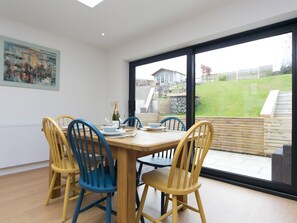 A dining area with a large table, four chairs, and a bottle of champagne. - Modern Welsh cottage moments from the beach - Pass the Keys (Pentraeth)