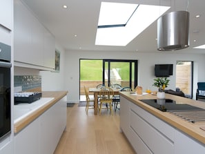 A modern kitchen with a skylight, a dining area with chairs, and a TV mounted on the wall. - Modern Welsh cottage moments from the beach - Pass the Keys (Pentraeth)