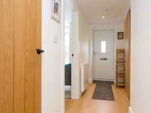 A hallway with a wooden door, a white door with a window, and a metal shelf unit. - Modern Welsh cottage moments from the beach - Pass the Keys (Pentraeth)