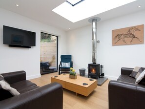 A modern living room with a fireplace, leather sofas, a wooden coffee table, and a TV mounted on the wall. - Modern Welsh cottage moments from the beach - Pass the Keys (Pentraeth)