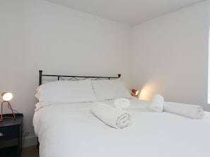 A neatly made bed with white linens and rolled towels, a black metal headboard, and bedside lamps on a nightstand. - Modern Welsh cottage moments from the beach - Pass the Keys (Pentraeth)