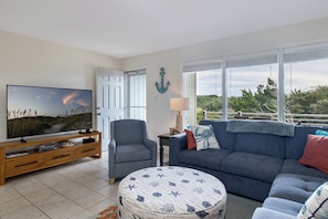 A living room with a television, a sofa, a chair, and a round ottoman. - Tar Landing Villas 306 - 3BR 2 BA - Oceanview Condo in Atlantic Beach (Atlantic Beach)