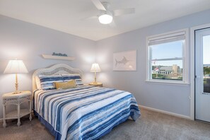 A bedroom with a bed, two nightstands, a ceiling fan, a window with a view, and a wall-mounted artwork. - Tar Landing Villas 306 - 3BR 2 BA - Oceanview Condo in Atlantic Beach (Atlantic Beach)