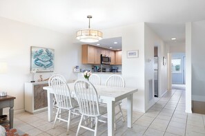 A modern kitchen with white cabinetry, a dining table with four chairs, and a pendant light. - Tar Landing Villas 306 - 3BR 2 BA - Oceanview Condo in Atlantic Beach (Atlantic Beach)
