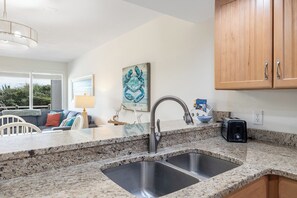 Cocina con encimeras de granito, pileta de acero inoxidable, armarios de madera y vista al área de estar.