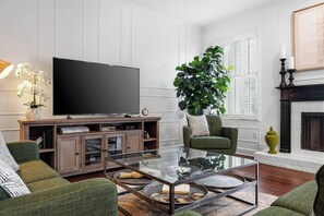 A living room with a flat-screen TV, a glass coffee table, green sofas, a large potted plant, and a fireplace. - Davis Islands 3BR | Walk to Dining (Tampa)