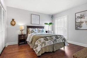 Un dormitorio con cama, mesita de noche, lámpara y una cita enmarcada en la pared.
