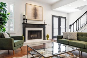 A modern living room with a fireplace, two green sofas, a glass coffee table, and a large abstract painting. - Davis Islands 3BR | Walk to Dining (Tampa)