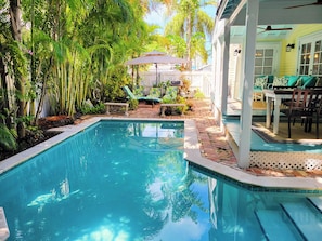 A swimming pool surrounded by lush greenery, with a patio area featuring outdoor furniture and a covered seating area. - Historic Seaport Retreat with Private Heated Pool & Guest Cottage (Key West)