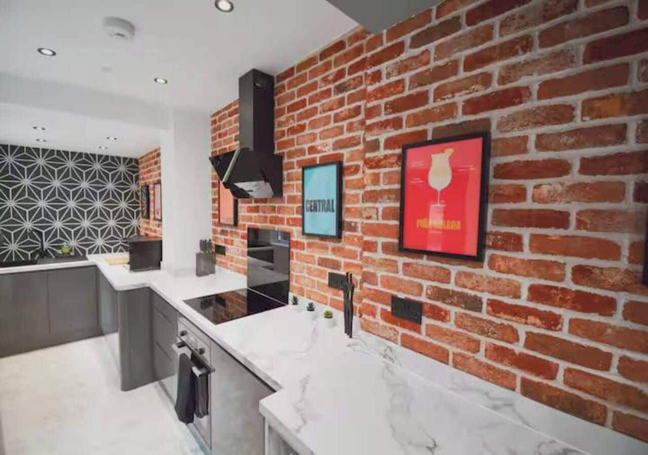 A modern kitchen with a brick wall backsplash, a white countertop, and a black range hood.