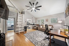 Ein modernes Wohnzimmer mit einer Couch, Sesseln, einem Couchtisch, einem Fernseher und einem Deckenventilator.