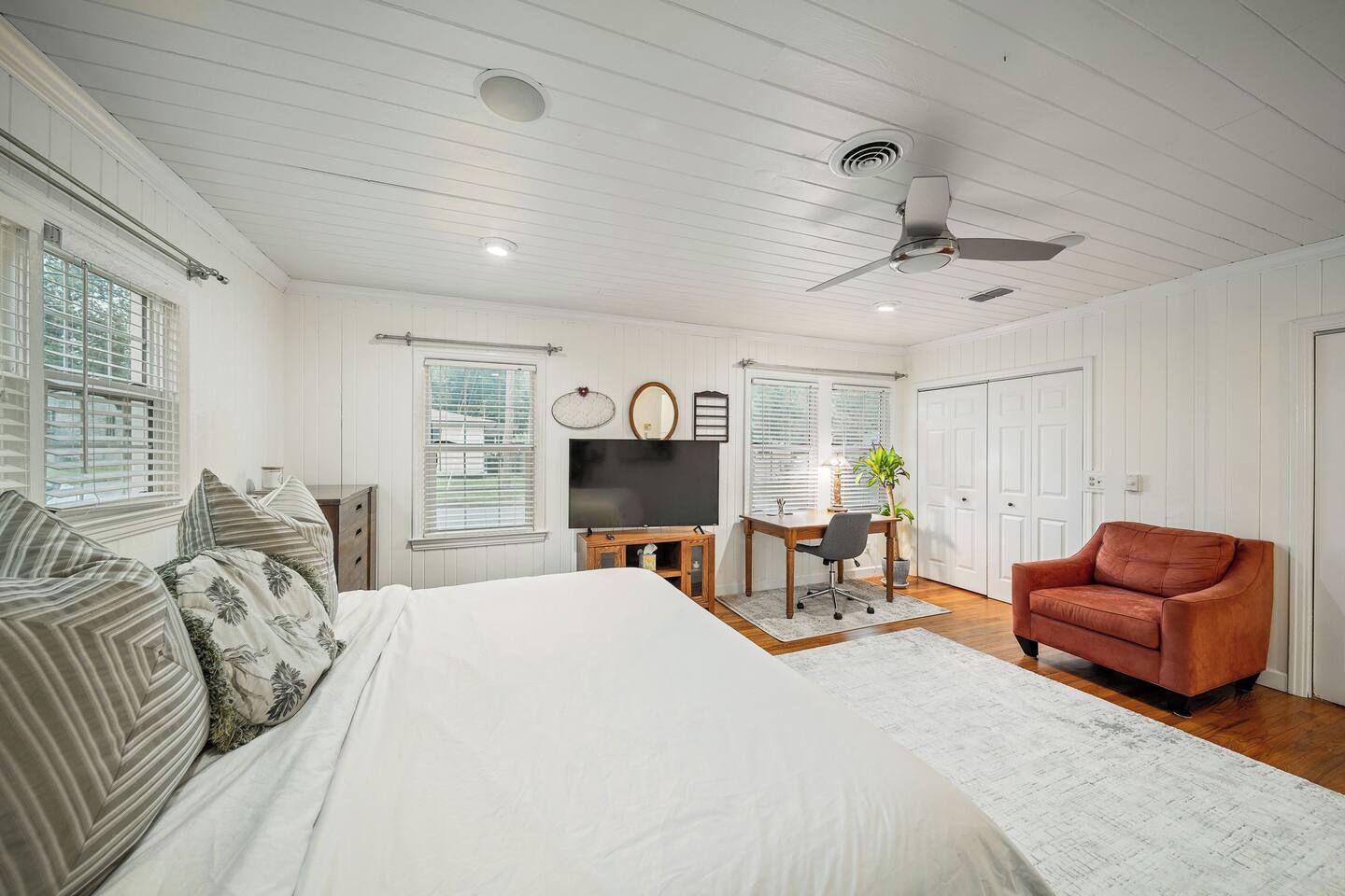 A bedroom with a bed, a desk, a chair, a television, and a ceiling fan.