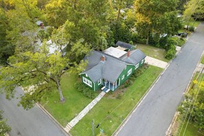 A green house with a covered porch, surrounded by trees and a driveway. - 3BR Movie Room | Walk to Dining (Tallahassee)