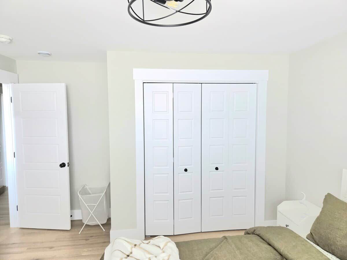 Ein Zimmer mit einem weißen Kleiderschrank, einem weißen Stuhl und einem Bett mit grüner Decke.