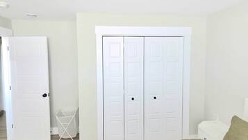 Ein Zimmer mit einem weißen Kleiderschrank, einem weißen Stuhl und einem Bett mit grüner Decke.
