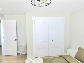 Ein Zimmer mit einem weißen Kleiderschrank, einem weißen Stuhl und einem Bett mit grüner Decke.