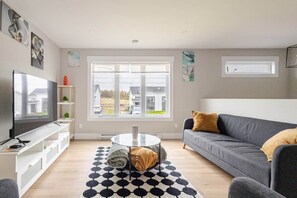 A modern living room with a flat-screen TV, a sofa, a coffee table, and a large window offering a view of the outside.