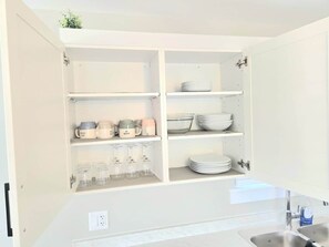 Une cuisine avec des placards ouverts où sont exposés la vaisselle, les verres et les boîtes de rangement.