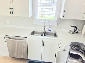 A modern kitchen with a stainless steel dishwasher, a double sink, and a coffee maker.