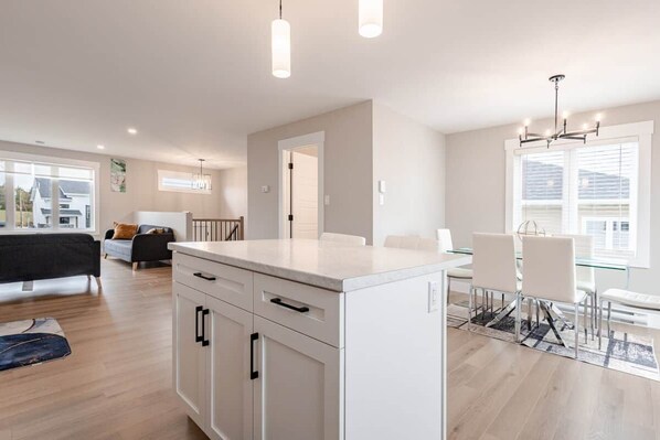 A modern kitchen with a central island, white cabinetry, and a dining area with a glass table and chairs.