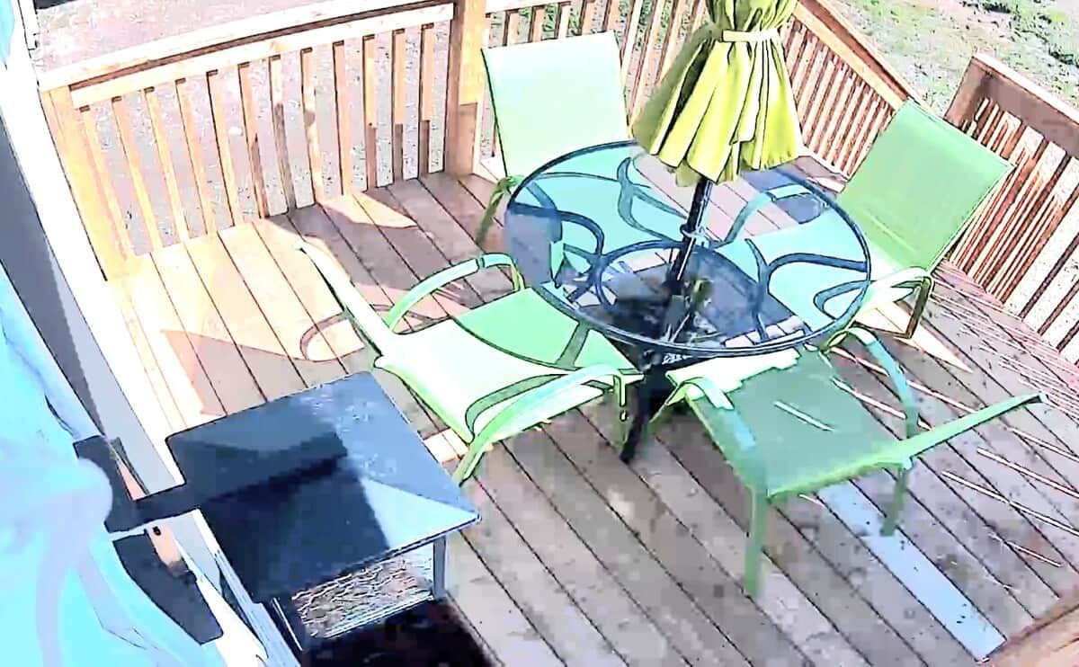 Eine Terrasse mit Glastisch und Stühlen, einem Grill und einem Holzzaun.