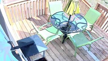 Eine Terrasse mit Glastisch und Stühlen, einem Grill und einem Holzzaun.