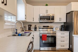 A modern kitchen with white cabinets, stainless steel appliances, a built-in oven, and a coffee maker.