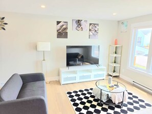 Un salon moderne avec un canapé, un téléviseur à écran plat, une table basse et un tapis à motifs.