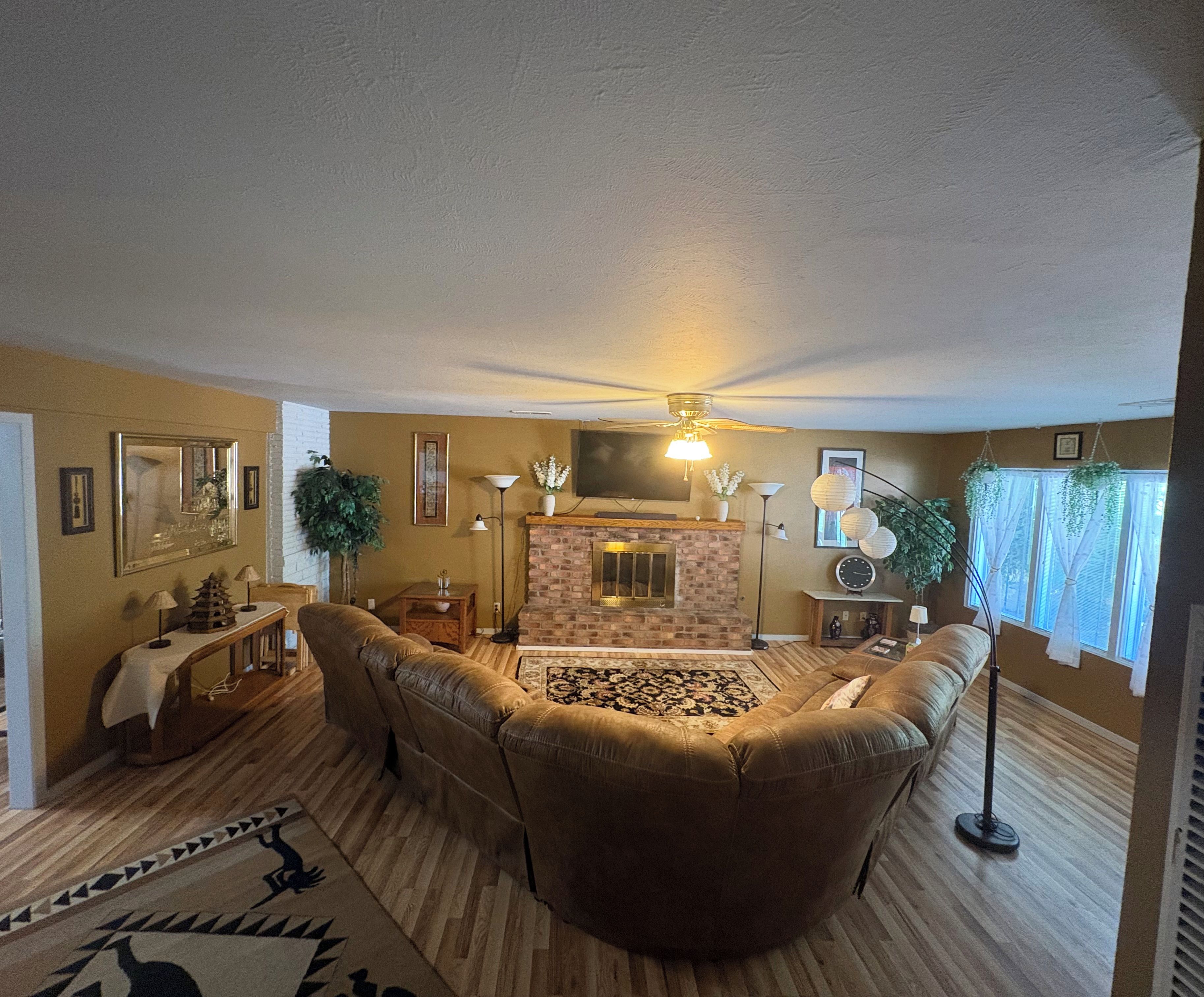 A living room with a fireplace, leather sofas, a ceiling fan, and a patterned rug.