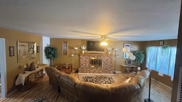 A living room with a fireplace, leather sofas, a ceiling fan, and a patterned rug.