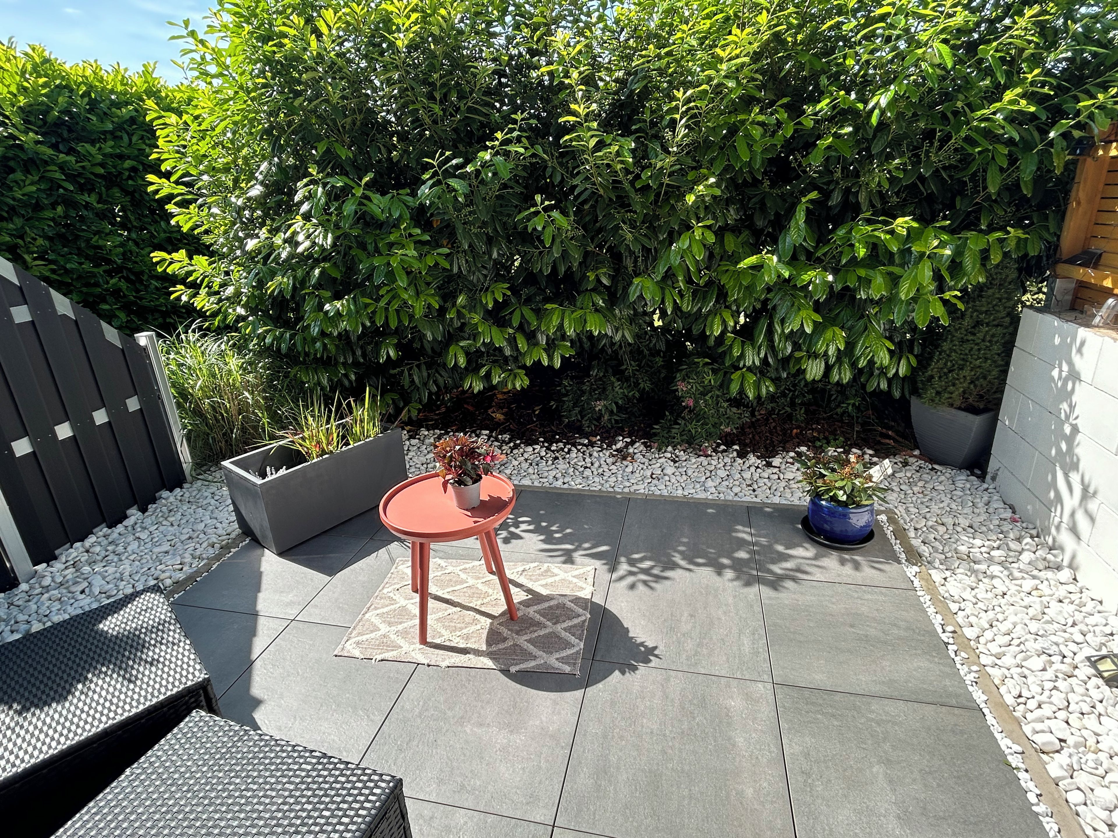 Eine Terrasse mit einem runden Tisch, einem Topfpflanzen und einer Sitzecke mit einem gemusterten Tischläufer.