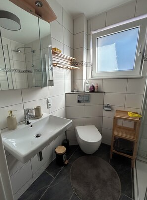 Un baño moderno con un espejo grande, un lavamanos, un inodoro y una cabina de ducha.