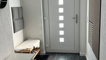 Un corridoio con una porta bianca, una panchina con un asciugamano, un appendiabiti e un tavolino.