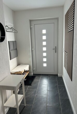 A hallway with a white door, a bench with a towel, a coat rack, and a small table.