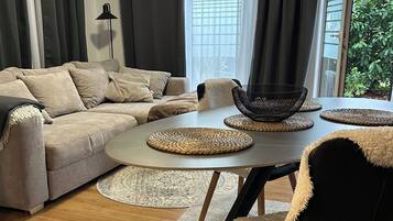 Una sala de estar moderna con un sofá modular, una mesa de comedor redonda con individuales tejidos, y vistas a la vegetación exterior.
