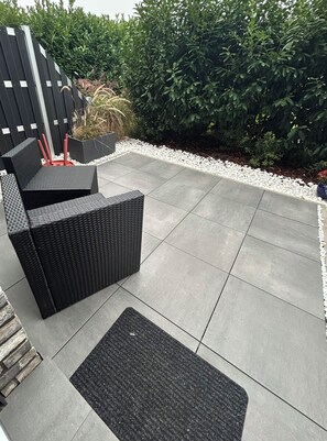 A patio area with a black wicker sofa, a small rug, and a white gravel border. - Vrbo Property (Vettweiss)