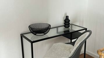 A modern room with a glass-top desk, a chair, a black vase, and a framed picture of the Eiffel Tower.
