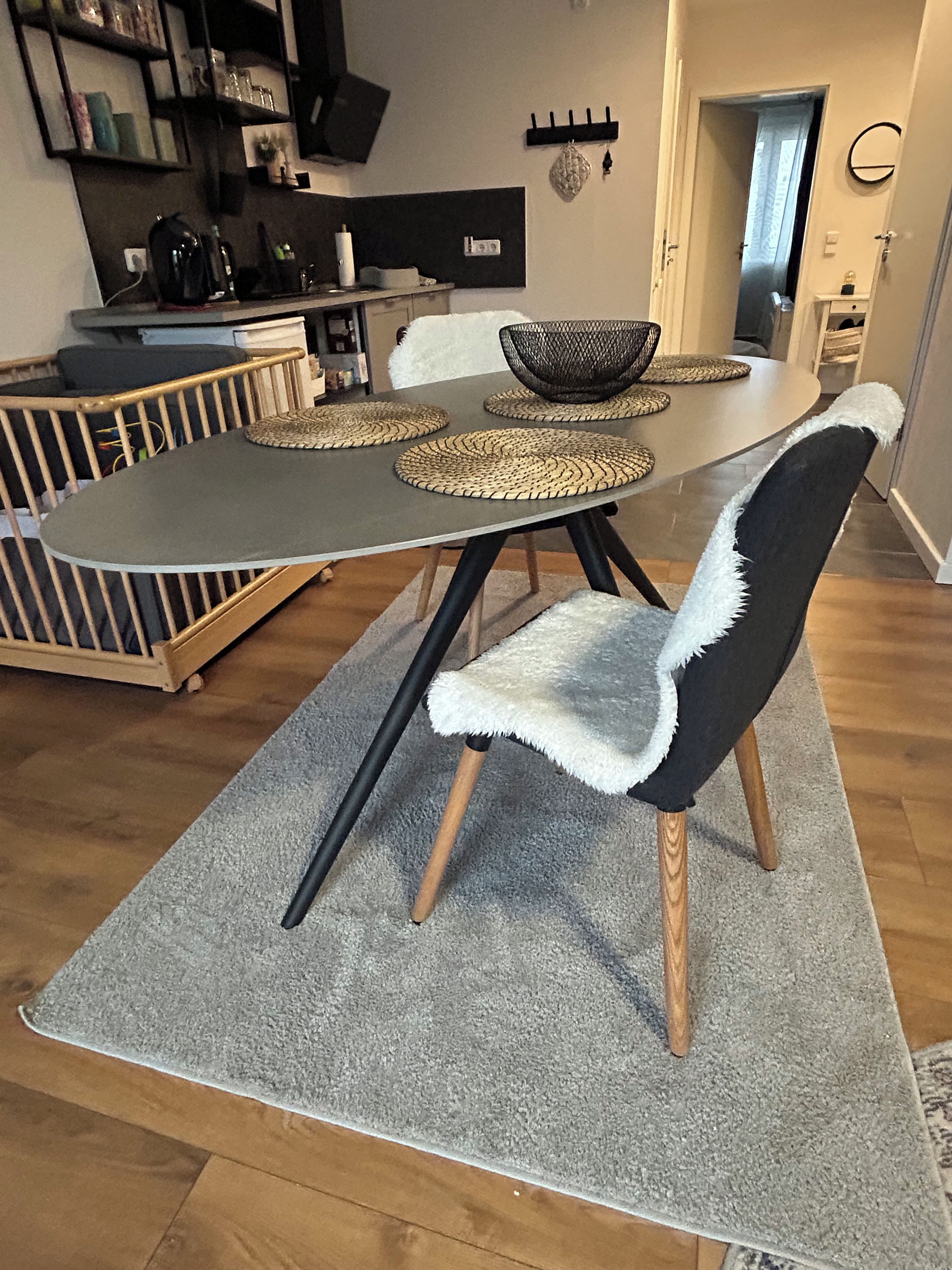 Un área de comedor con una mesa dispuesta para cuatro, rodeada de sillas con adornos de piel blanca.