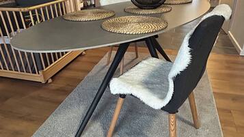 Un área de comedor con una mesa dispuesta para cuatro, rodeada de sillas con adornos de piel blanca.
