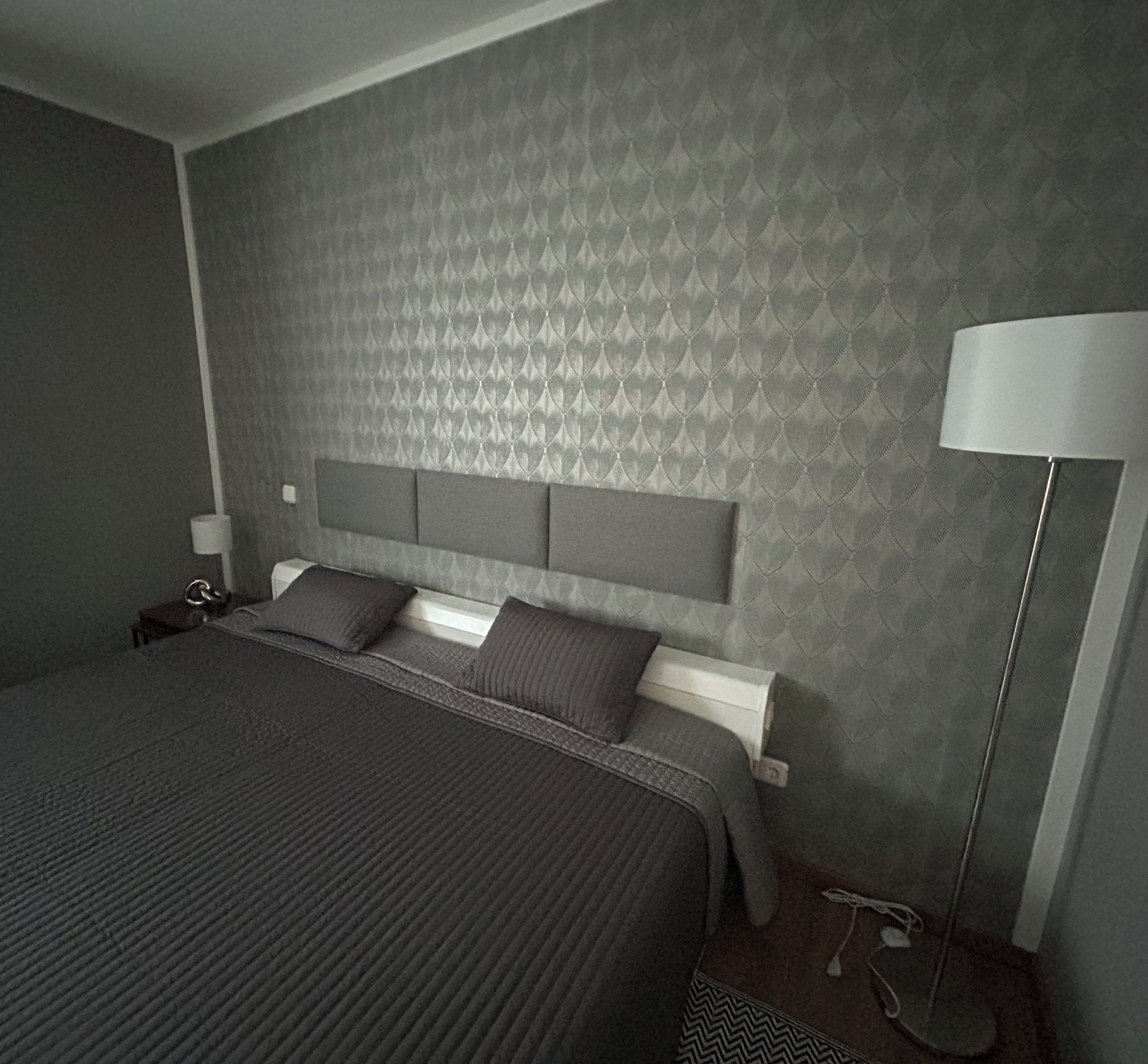 A modern bedroom with a large bed, a headboard, a bedside table, and a floor lamp.
