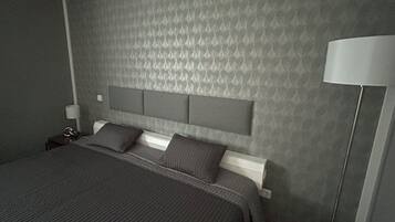 A modern bedroom with a large bed, a headboard, a bedside table, and a floor lamp.