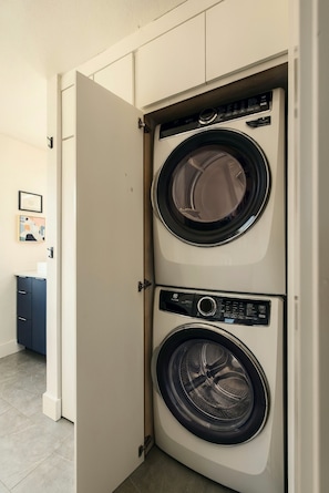 A laundry room with two stacked front-loading washing machines. - The Coler Treehouse - Steps to MTB Trails, 1 Mi to Downtown Bentonville (Bentonville)